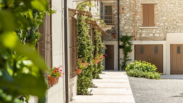 Un vicolo stretto fiancheggiato da edifici, con muri in pietra, persiane in legno e piante in vaso.