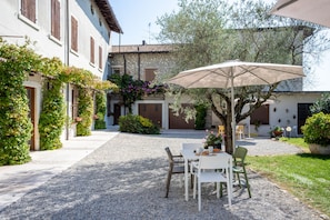 A courtyard with a gravel path, a table with chairs, and an umbrella. - Palazzo Trevignane San Felice del Benaco (San Felice del Benaco)