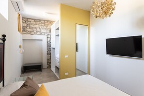 A bedroom with a bed, a television mounted on the wall, and a stone wall in the background. - Palazzo Trevignane San Felice del Benaco (San Felice del Benaco)