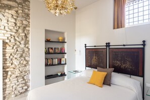 A bedroom with a stone wall, a bed with a wooden headboard, a bookshelf, and a hanging light fixture. - Palazzo Trevignane San Felice del Benaco (San Felice del Benaco)