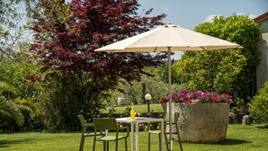 A garden patio with a table and chairs, a large umbrella, and potted plants.