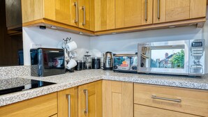 A kitchen with wooden cabinets, a granite countertop, a toaster, a kettle, a coffee maker, and a microwave. - Modern 3-Bed House | Wednesbury | Garage + Driveway (Wednesbury)