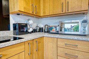A kitchen with wooden cabinets, a granite countertop, a toaster, a kettle, a coffee maker, and a microwave. - Modern 3-Bed House | Wednesbury | Garage + Driveway (Wednesbury)