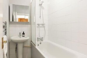 A bathroom with a white sink, mirror, and bathtub. - New! Lovely 1BR Flat w/ Patio in Herne Hill (Greater London)