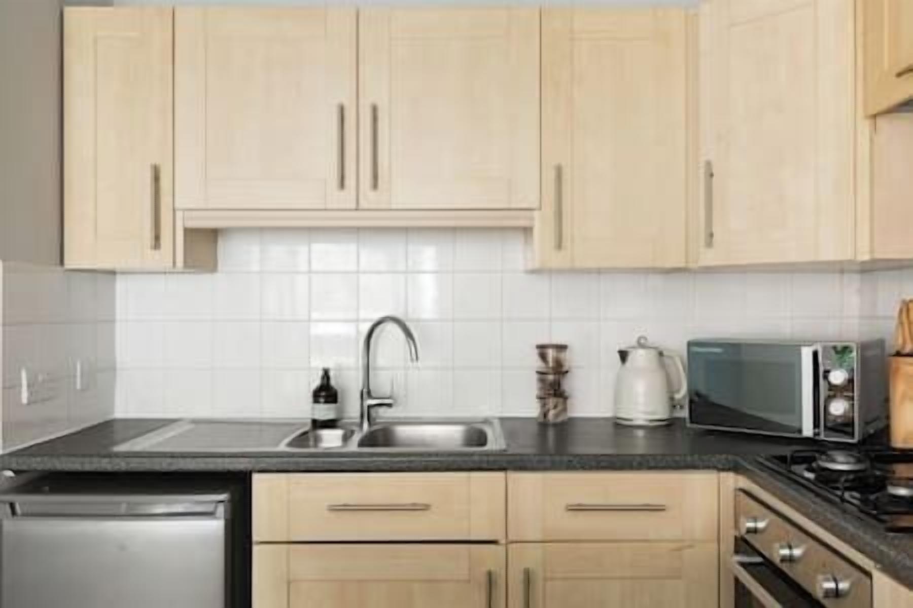 Une cuisine avec des meubles de couleur bois clair, un évier en acier inoxydable, un four à micro-ondes et une cuisinière.
