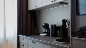 Et moderne køkken med hvide skabe, en indbygget ovn og en kaffemaskine på bordet.