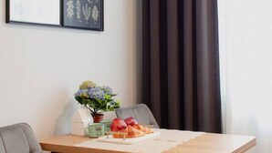 Et spiseområde med et træbord, to stole, en vase med blomster og et indrammet billede på væggen.