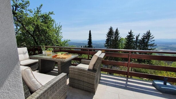 Un balcon agrémenté de meubles en osier, d’une table et offrant une vue sur les arbres et le paysage environnant.
