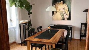 A dining area with a wooden table, black chairs, a black placemat, a vase with flowers, and a painting on the wall. - Seeliebe | city location | seeglueck (Konstanz)