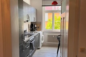 A compact kitchen with stainless steel appliances, a window with blinds, and a radiator. - Seeliebe | city location | seeglueck (Konstanz)