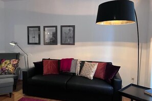A modern living room with a black sofa, a floor lamp, and three framed pictures on the wall. - Seeliebe | city location | seeglueck (Konstanz)