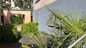 A courtyard with a table and chairs, a metal fence, and a building with a grey wall and a beige archway. - Seeliebe | city location | seeglueck (Konstanz)