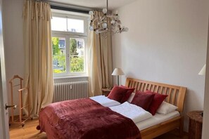 Ein Schlafzimmer mit einem hölzernen Bett, cremefarbenen Vorhängen, einem Fenster mit Blick und einer Pendelleuchte.