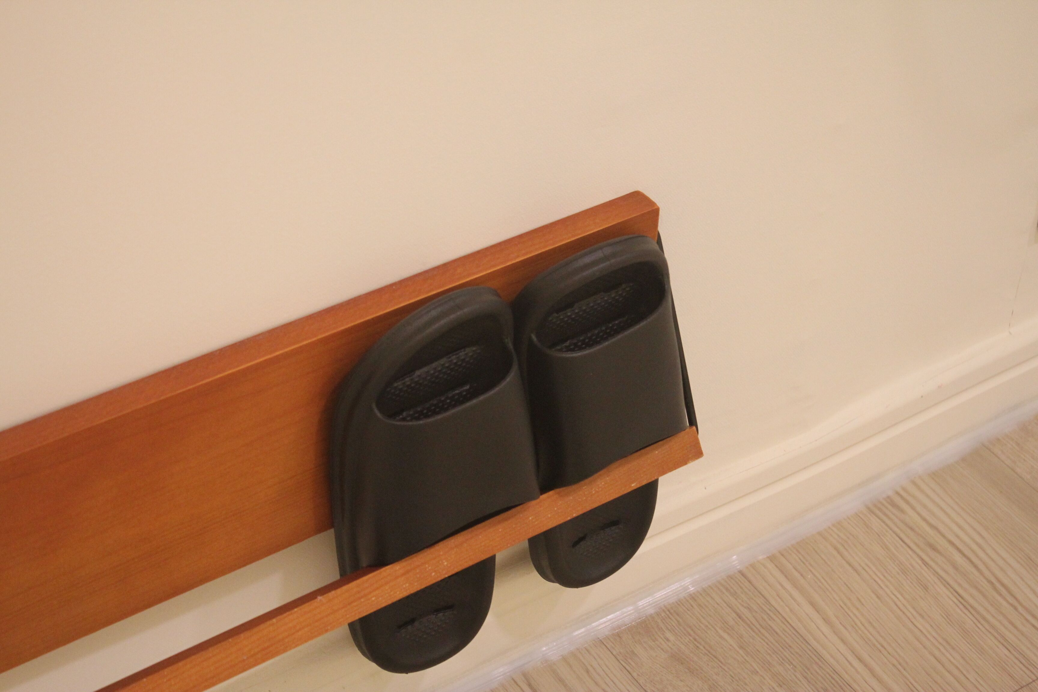 A pair of black slippers on a wooden shelf against a wall.