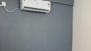Una cama individual con cabecera de madera, una mesita con una toalla blanca doblada y un equipo de aire acondicionado en la pared.