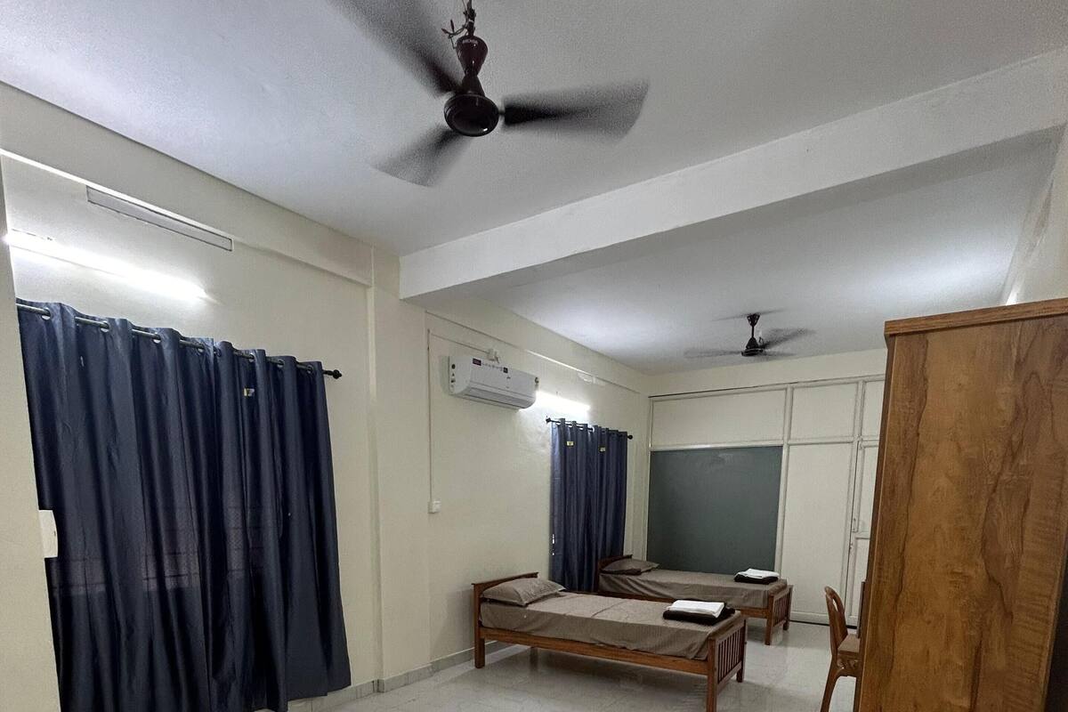 Une pièce spacieuse comprenant un lit, un bureau, une armoire et un ventilateur de plafond.