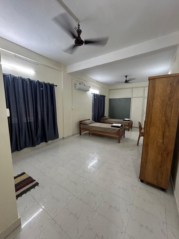 A spacious room with a bed, a desk, a wardrobe, and a ceiling fan. - TGM INN (Kottayam)