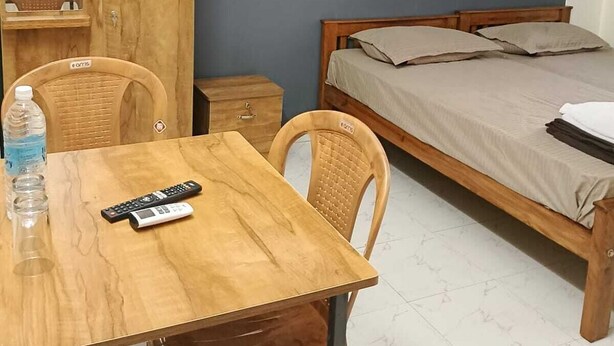 Una habitación pequeña y sencilla con una mesa de madera, dos sillas, una cama, un armario y un espejo.