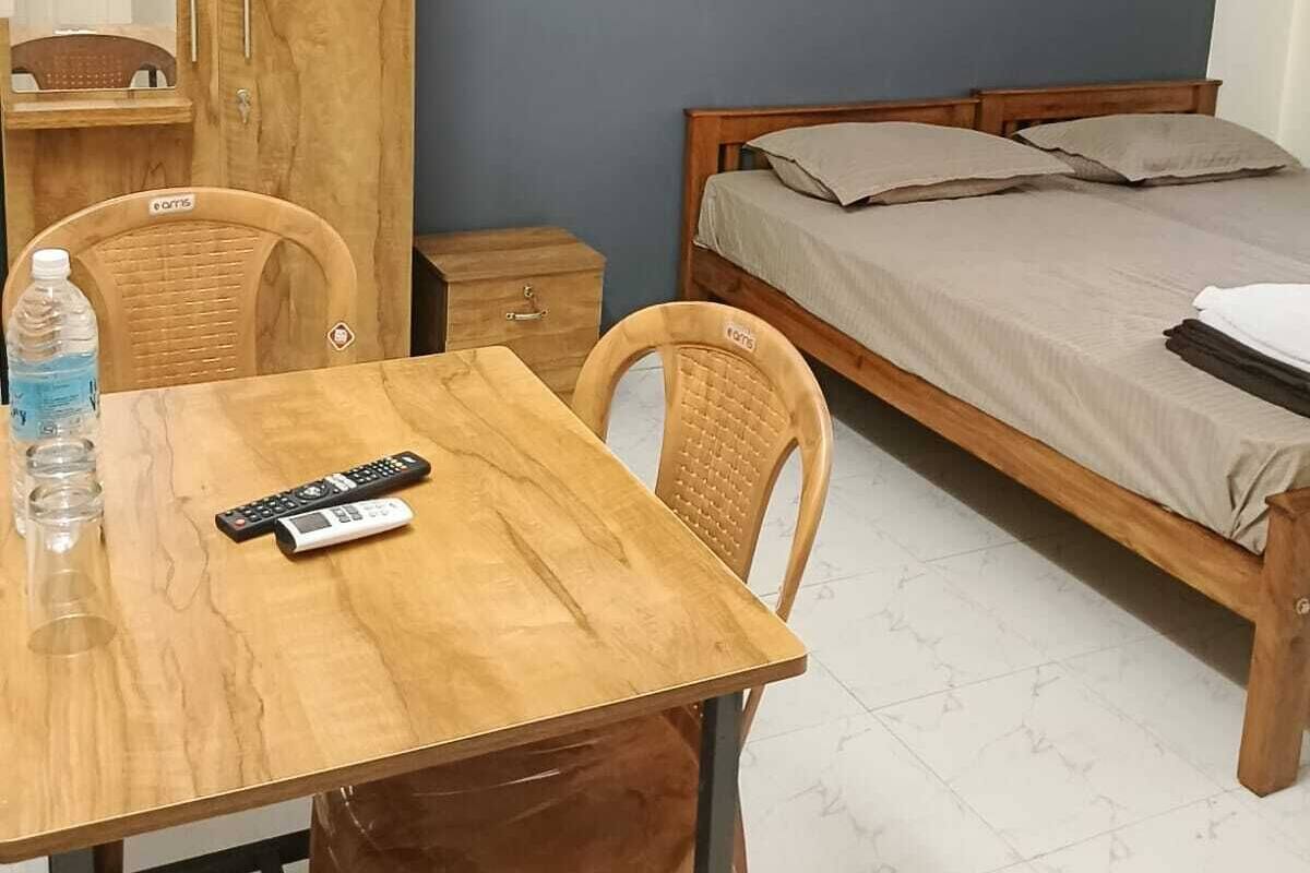 Une petite pièce simple, avec une table en bois, deux chaises, un lit, une armoire et un miroir.