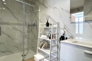 Ein modernes Badezimmer mit einer gläsernen Duschkabine, einer weißen Marmorwand und einer eingebauten Ablage mit Pflegeprodukten.