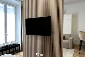 Ein moderner Raum mit einem großen Fernseher an einer lamellenverkleideten Wand, einer Bank am Fenster, einer Couch und einem Essbereich.