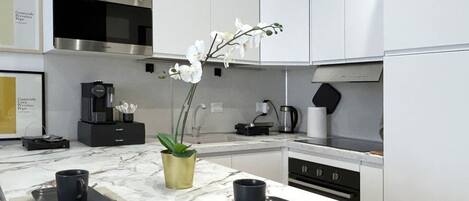 A modern kitchen with a marble countertop, a coffee machine, a microwave, and a sink.