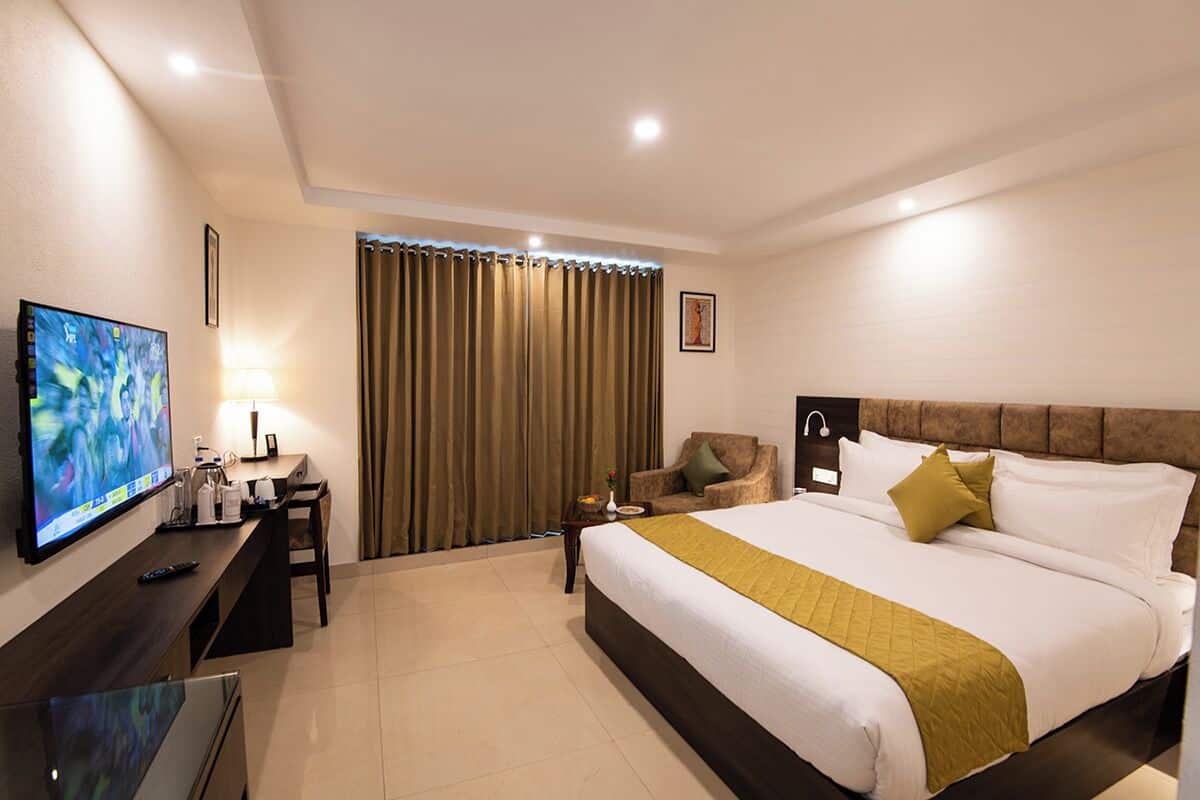 A hotel room with a bed, a TV, a desk, a chair, and a window with curtains.