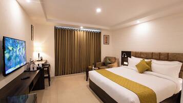 Habitación de hotel con cama, televisor, escritorio, silla y ventana con cortinas.
