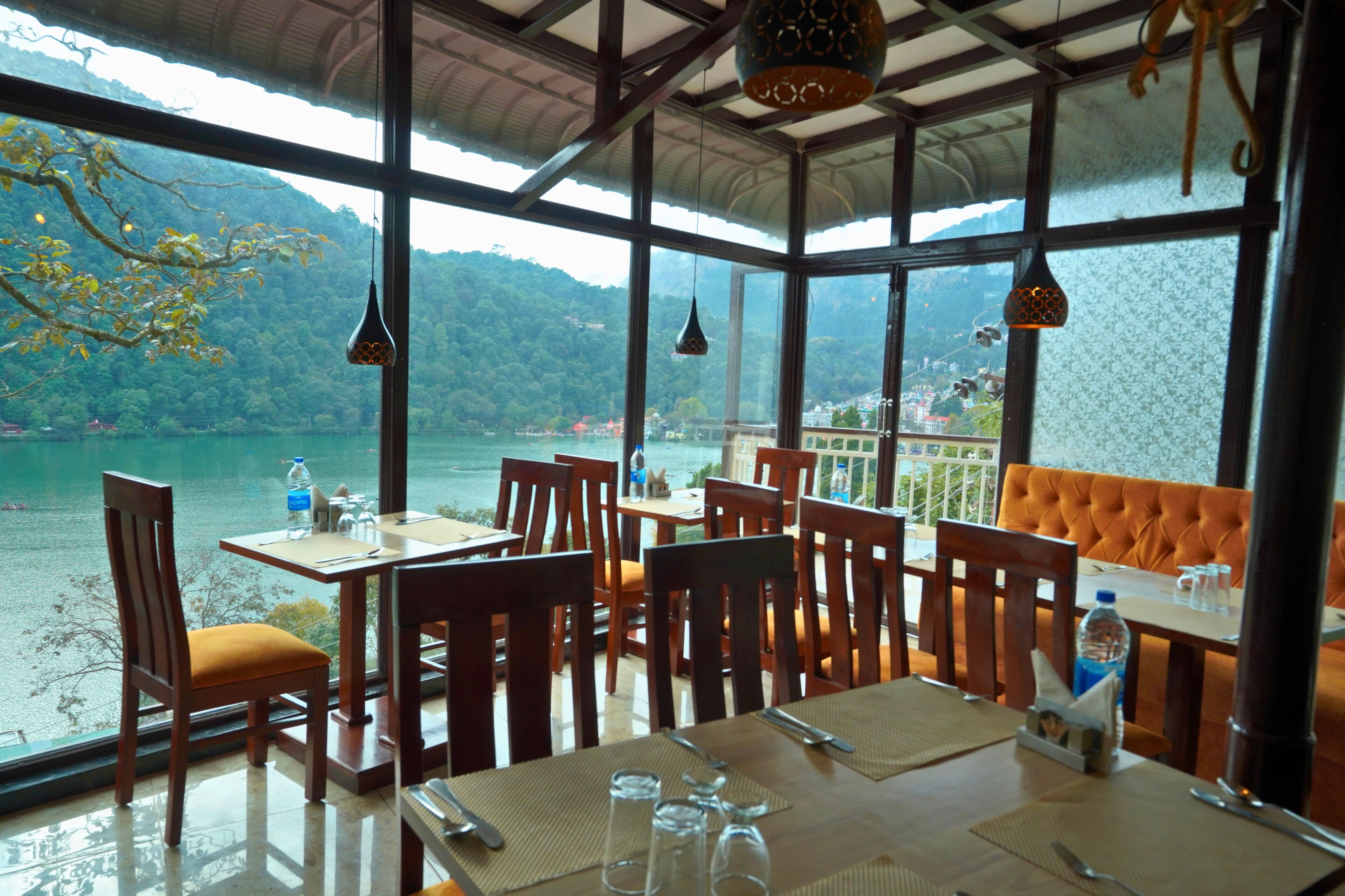 A restaurant with tables and chairs, a view of a lake, and hanging light fixtures.