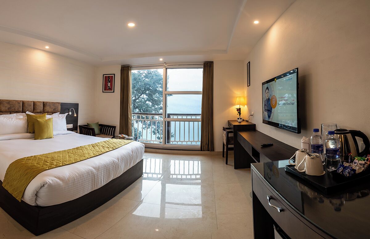 A hotel room with a bed, a desk, a TV, and a balcony with a view.