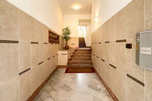 Ein Hotelgang mit Marmorboden, einer Treppe, einer Topfpflanze und einem an der Wand befestigten Thermostat.