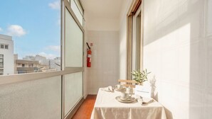Ein Balkon mit einem für Tee gedeckten Tisch, einem Feuerlöscher und Blick auf Gebäude.