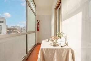 Ein Balkon mit einem für Tee gedeckten Tisch, einem Feuerlöscher und Blick auf Gebäude.