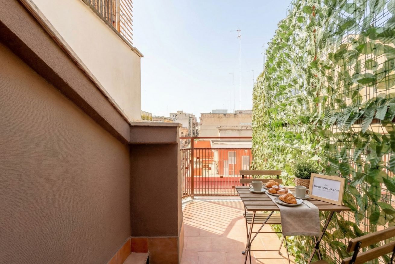 Een balkon met een ontbijttafel, een bloempot en een lijst met foto.