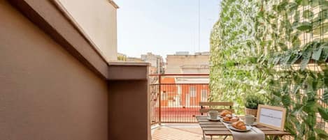 A balcony with a table set for breakfast, a potted plant, and a framed picture.