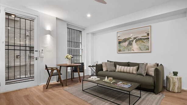 A living room with a sofa, coffee table, and a painting on the wall. - Laneway Living | 1BR Heritage Stay in CBD (Melbourne)