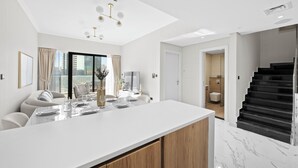 Una cocina moderna con una isla grande, un comedor con sillas y una mesa, y una escalera que sube a un nivel superior.