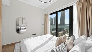 Una habitación de hotel moderna con una cama grande, un espejo redondo, vistas a la ciudad y un balcón con mobiliario exterior.