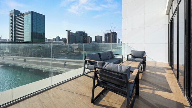Una terraza moderna en la azotea con barandilla de vidrio, dos sofás y una mesa de madera.
