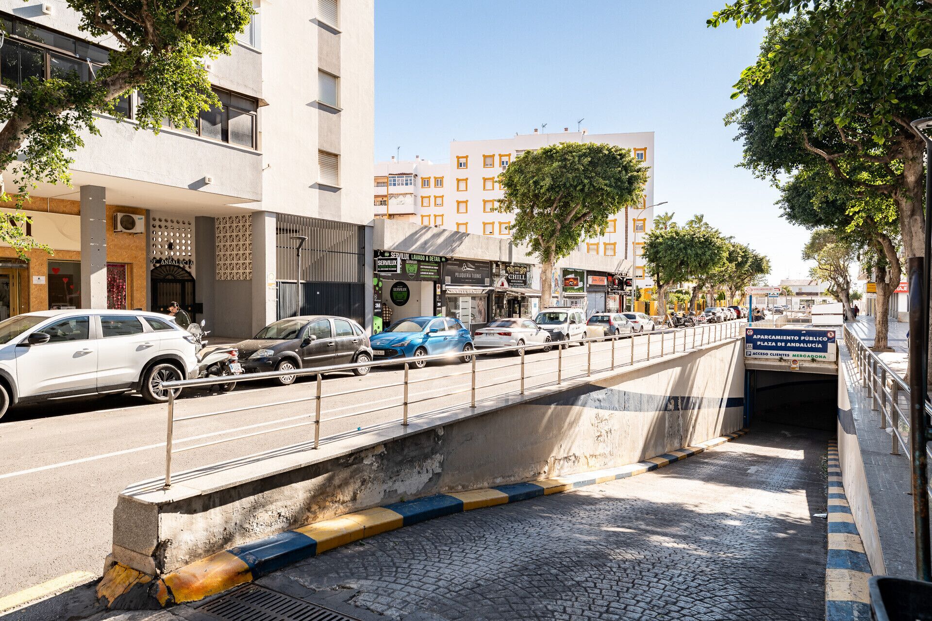 A pedestrian bridge over a cobblestone street with cars parked on the side.