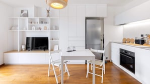 Una cocina moderna con armarios blancos, una mesa de comedor con sillas, un horno empotrado y un refrigerador grande.