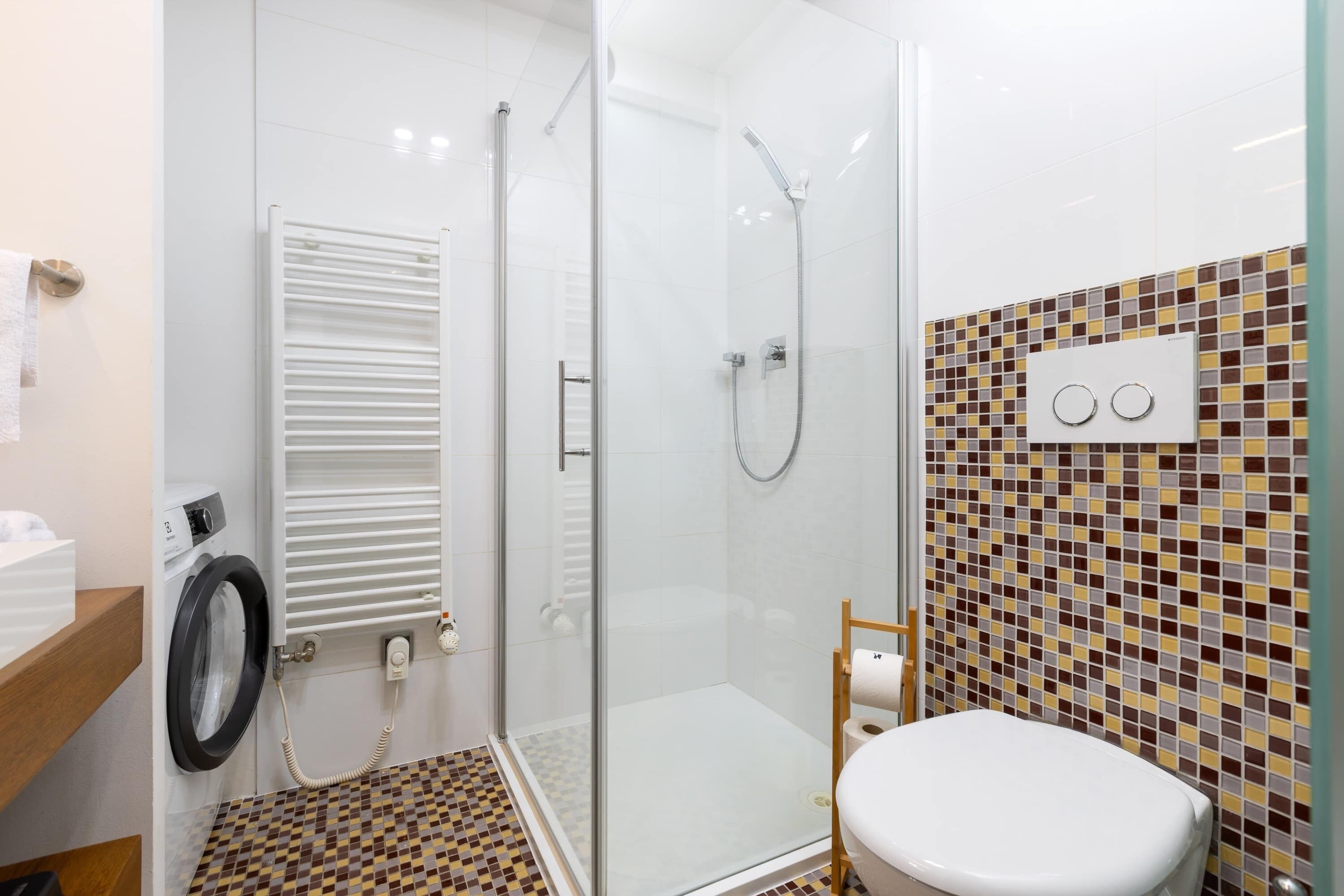 Un baño moderno con ducha acristalada, inodoro y lavadora.