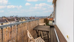 Un balcón con mesa y sillas de madera, una valla de bambú y vistas de la ciudad.