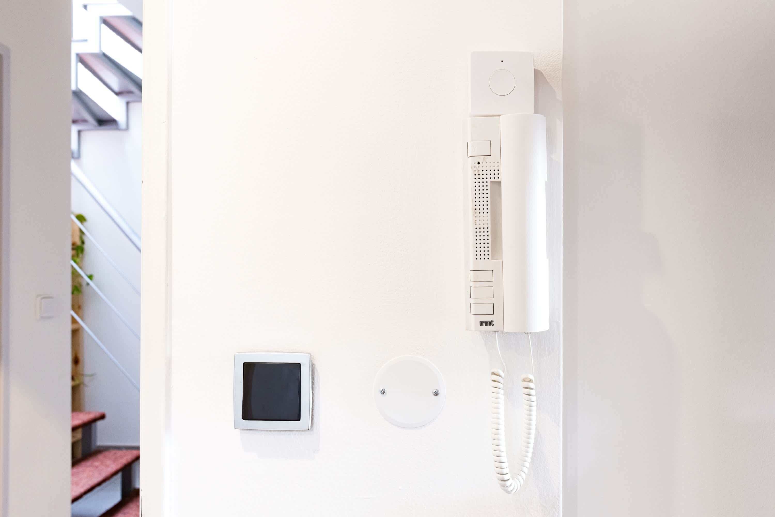 A white wall-mounted telephone, a small digital screen, and a round vent.