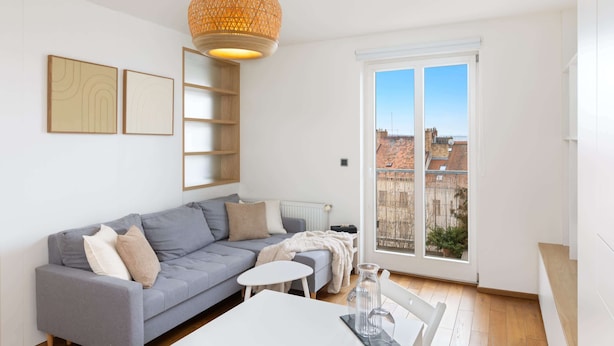 Una sala de estar moderna con un sofá gris, una mesita blanca y un ventanal con vistas a edificios.