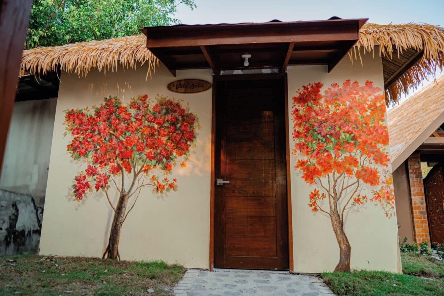 A building with a wooden door, a thatched roof, and two trees painted on the wall.