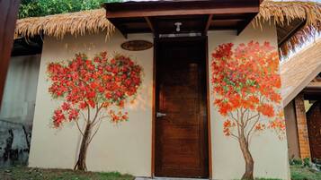 A building with a wooden door, a thatched roof, and two trees painted on the wall.