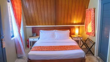 Ein Schlafzimmer mit Holzbalkendecke, einem Bett mit weißer Bettwäsche, einem Nachttisch, einer Lampe und einem Fenster mit orangefarbenen Vorhängen.