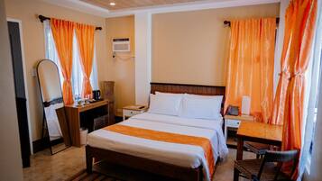 A hotel room with a bed, bedside table, chair, desk, and a mirror.