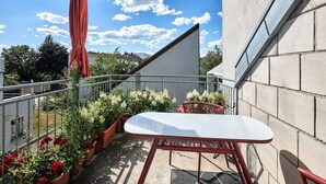 Un balcon avec une table et des chaises, des plantes en pot et un parasol rouge.